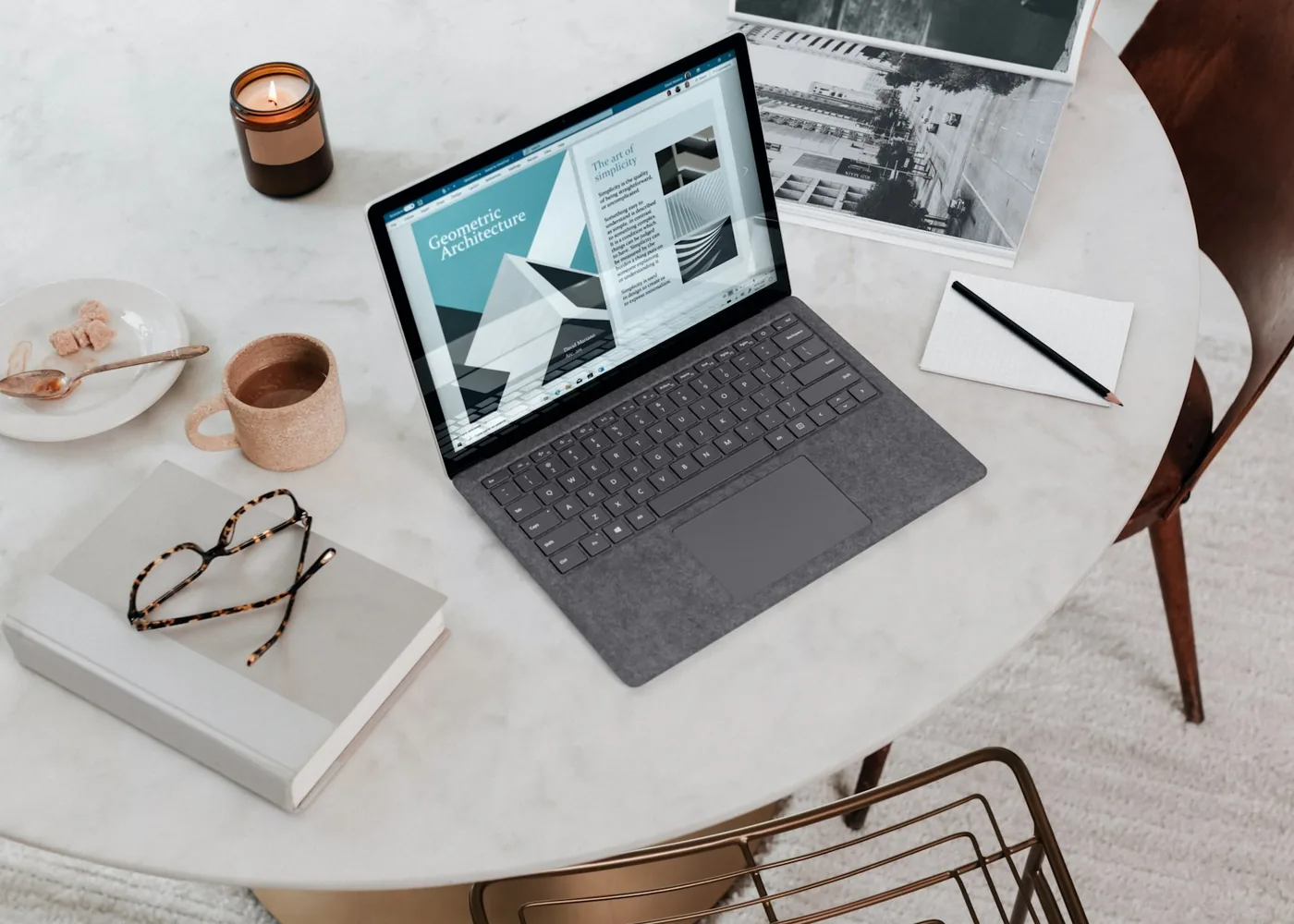 A laptop open on a bright table with a coffee cup and notebook